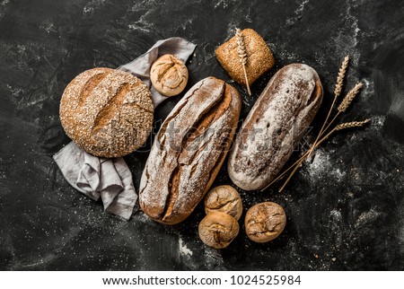 Bakery - gold rustic crusty loaves of bread and buns on black chalkboard background. Still life captured from above (top view, flat lay).