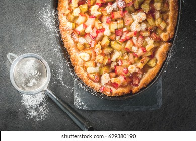 Bakery. Ready freshly baked homemade pie with rhubarb and sugar. Shortbread. Rustic style. On a stone black table. With sugar powder for sprinkling. Top view,  copy space - Powered by Shutterstock