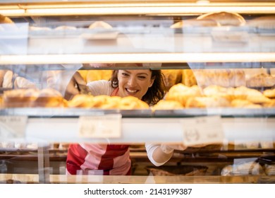 Bakery seller arranging freshly baked pastry products on shelf in bakery shop. - Powered by Shutterstock