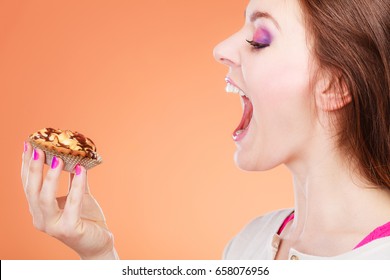 Bakery, Sweet Food And People Concept. Woman Face Profile Wide Open Mouth Holds Cake Cupcake In Hand Orange Background