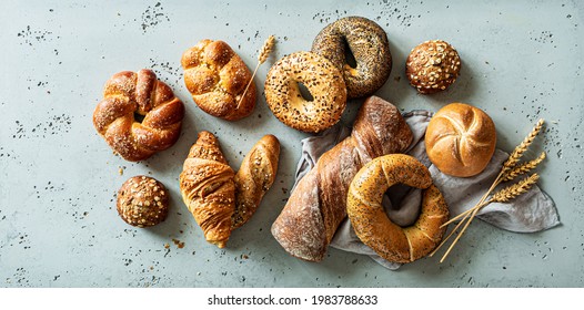 Bakery - various kinds of breadstuff. Bread rolls, bagel, sweet bun and croissant captured from above (top view, flat lay). Grey stone background.