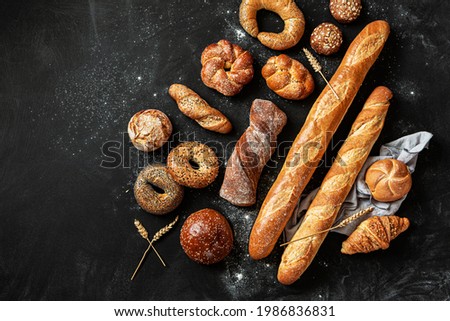 Bakery - various kinds of breadstuff. Bread rolls, baguette, bagel, burger bun and croissant captured from above (top view, flat lay). Black chalkboard background with free copy (text) space.