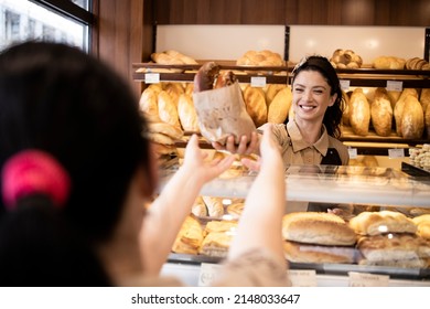 Bakery worker selling fresh tasty pastry and bread in bakery shop.