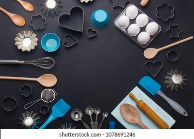 Baking background with eggs and kitchen tools: rolling pin, wooden spoons, whisk, sieve, bakeware and shape cookie cutter on dark wooden background. Horizontal orientation with copyspace, top view.
