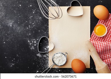 Baking background with flour, rolling pin, eggs, paper sheet and heart shape on kitchen black table from above for Valentines day cooking. Flat lay style - Powered by Shutterstock