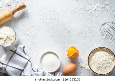 Baking background ingredients. Flour, sugar, eggs and rolling pin at light stone table.