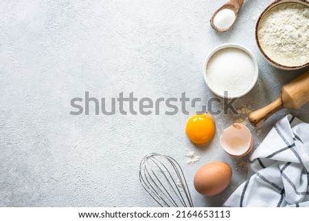 Baking background ingredients. Flour, sugar, eggs and rolling pin at light stone table.
