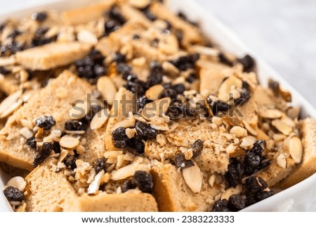 Baking bread pudding with raising and almond slivers in a white casserole dish.