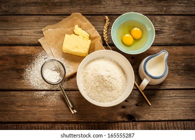 Baking cake in rural kitchen - dough recipe ingredients (eggs, flour, milk, butter, sugar) on vintage wood table from above - Powered by Shutterstock