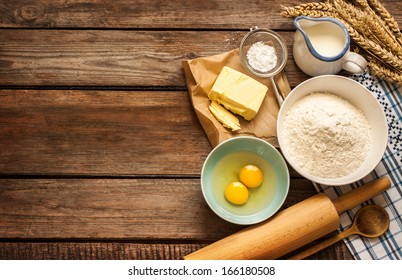 Baking cake in rural kitchen - dough recipe ingredients (eggs, flour, milk, butter, sugar) and rolling pin on vintage wood table from above. Rustic background with free text space. - Shutterstock ID 166180508
