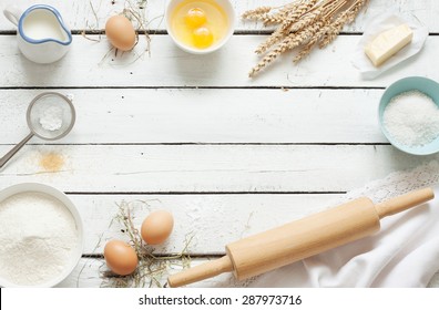 Baking cake in rustic kitchen - dough recipe ingredients (eggs, flour, milk, butter, sugar) on white planked wooden table from above. Background layout with free text space.