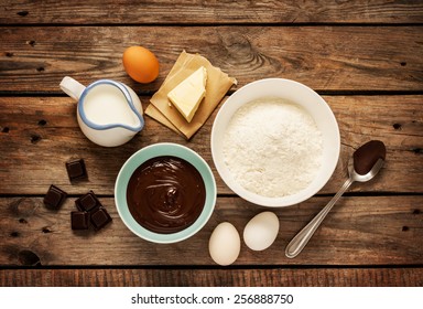 Baking Chocolate Cake In Rural Or Rustic Kitchen. Dough Recipe Ingredients (eggs, Flour, Milk, Butter) On Vintage Wood Table From Above.