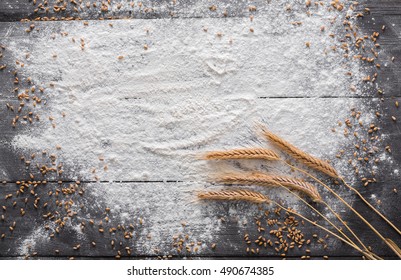 Baking class or recipe concept on dark background, sprinkled wheat flour, grain and ears with free copy space. Top view on wooden board or table. Cooking dough or pastry.