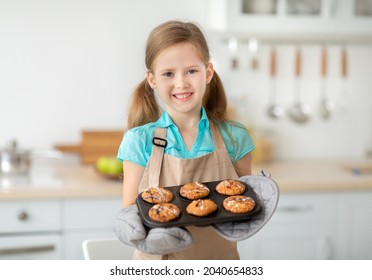 Baking Concept. Portrait Of Smiling Cute Little Girl Holding Tray With Freshly Baked Cookies Muffins. Positive Kid Wearing Apron, Preparing Homemade Cakes For Mother's Day. Granny's Recipe