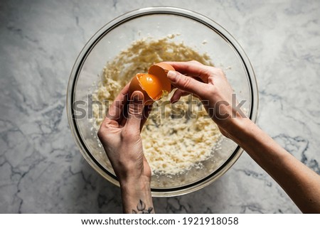 Baking cookies. Adding an egg into a mixture of butter and sugar in a big glass bowl. Top view horizontal photo.