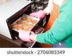 Baking cookies in the kitchen using a microwave oven while wearing colorful oven mitts