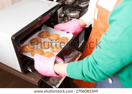 Baking cookies in the kitchen using a microwave oven while wearing colorful oven mitts