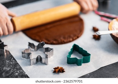 baking, cooking and christmas concept - close up of molds and hands rolling gingerbread dough with rolling pin on black kitchen table top