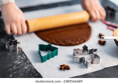 baking, cooking and christmas concept - close up of molds and hands rolling gingerbread dough with rolling pin on black kitchen table top
