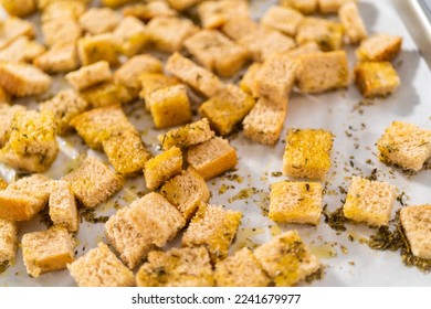 Baking croutons seasoned with olive oil and spiced on a baking sheet lined with parchment paper.