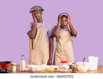 Baking Disaster Concept. Desperate Young Black Couple Having Difficulty Cooking Over Lilac Background. Young Woman And Her Boyfriend Are In Trouble, Cannot Prepare Homemade Meals