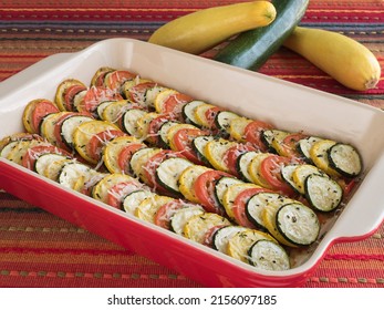 A Baking Dish Of Alternating Zucchini, Yellow Squash, And Tomato Circles, Topped With Parmesan Cheese And Garnished With Fresh Rosemary And Thyme 