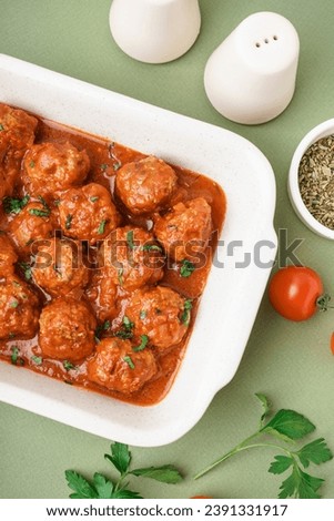 Baking dish of tasty meat balls with tomato sauce and parsley on green background