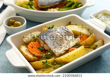 baking dish of tasty sea bass fish with vegetables on blue background