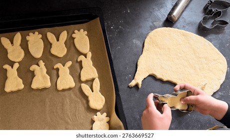 Baking Easter cookies with various shaped dough cutouts on a baking tray and a rolling pin on a home kitchen setting