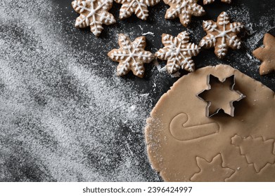 Baking gingersnap at home. Rolled dough with snowflake, Christmas tree, cane ornaments from cookie cutters, baked snowflake cookie with sugar glaze on table background with flour, copy space. - Shutterstock ID 2396424997