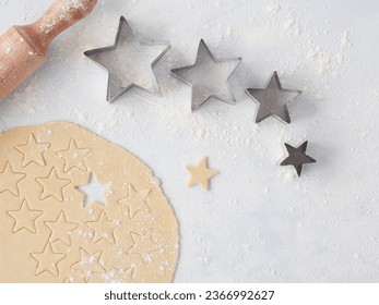 Baking at home for Christmas, dough cut with star-shaped pastry cutters of different sizes. Wooden rolling pin on the table seen from above. - Powered by Shutterstock