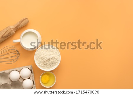 Baking Ingredient- flour, egg, milk, rolling pin, whisk on a pastel yellow background. Top view, flat lay, copy space.
