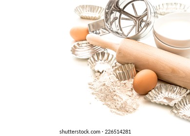 Baking Ingredients And Tolls For Dough Preparation. Flour, Eggs, Rolling Pin And Cookie Cutters On White Background