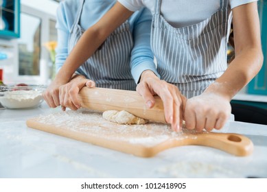 Baking with joy. Loving sweet little daughter making some dough and her mom helping her and they wearing aprons - Shutterstock ID 1012418905