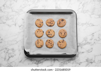 Baking pan with cookies and parchment paper on white marble table, top view