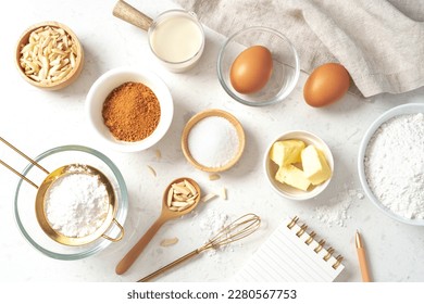 Baking pastry or cake ingredients, sugar, flour, eggs and milk with notebook and pen on marble table, top view - Shutterstock ID 2280567753