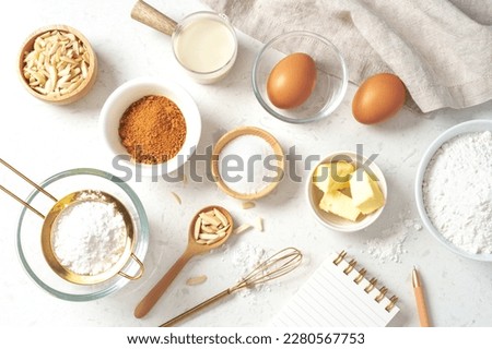Baking pastry or cake ingredients, sugar, flour, eggs and milk with notebook and pen on marble table, top view