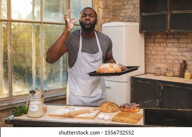 Baking process. Cheerful dark skinned African American male wears apron, kneads dough with great enthusiasm, being content to recieve praise from chef for endeavour and hard work in restaurant.
