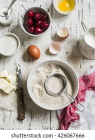 Baking rustic light background. Raw ingredients for baking pie with cherries - flour, eggs, milk, sugar, butter, cream, cherries.  Rustic style