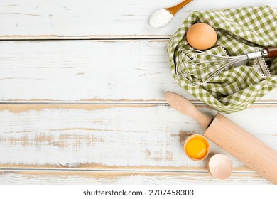 Baking setup with mixing tools, eggs, and flour on a wooden table in a kitchen