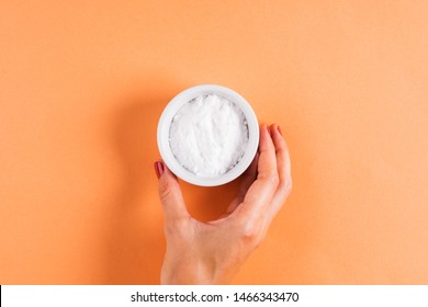 Baking Soda In Bowl On Orange Background. Woman's Hand Holding The Bowl. Concept Of Baking Soda As Multi Use Cleaning Or Beauty Ingredient