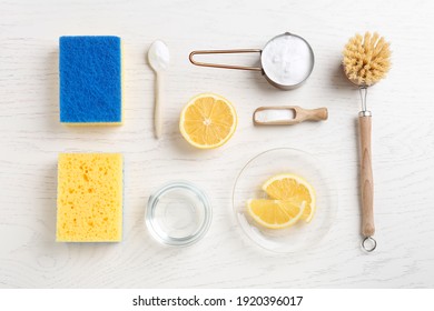Baking soda, vinegar, lemon, cleaning brush and sponges on white wooden table, flat lay