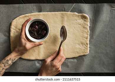 Baking Sweet Cottage Cheese Braided Bread With Raisins And Jam. Rolled Out Dough On The Parchment Paper, Female Hands Holding A Bowl Of Jam And A Spoon. Overhead Shot.