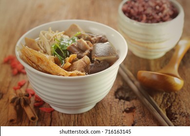 Bak-kut-teh is a pork rib dish cooked in broth popularly served in Malaysia and Singapore and Southern Thailand. Chinese hot soup with herbs on rustic wood. 