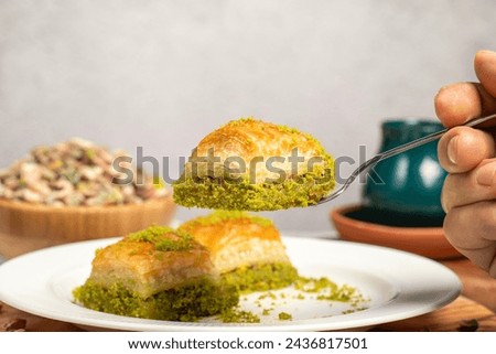 Baklava with pistachios on a wooden background. Turkish cuisine delicacies. Ramadan Dessert. He is holding a slice of baklava on the fork. local name kuru baklava