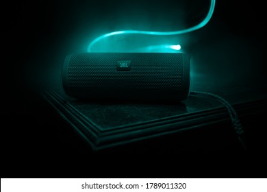 BAKU. AZERBAIJAN - 28.07.2020: JBL Flip 4 Bluetooth Speaker close up shot on wooden table with colorful lights and fog on background. Selective focus