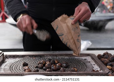 Baku, Azerbaijan - January 03 2022-  Roasted Chestnut Seller Stuffing Chestnuts In A Paper Bag, Hand
 With Motion Blur.