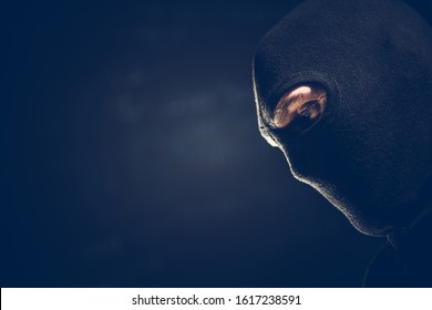 Balaclava Masked Robber Portrait. Caucasian Terrorist or Theft Wearing Black Face Mask. Left Side Copy Space. Dark Theme.