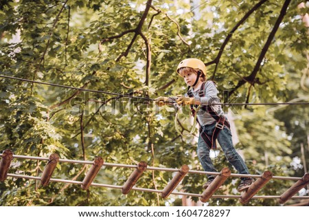 Balance beam and rope bridges. Go Ape Adventure. Child concept. Climber child on training. Portrait of a beautiful kid on a rope park among trees. Carefree childhood.