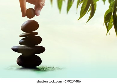Balance concept between of Life and work present by Hand setting a natural zen rock stone stack, Surrounded with Leaf and Ripple, Side view